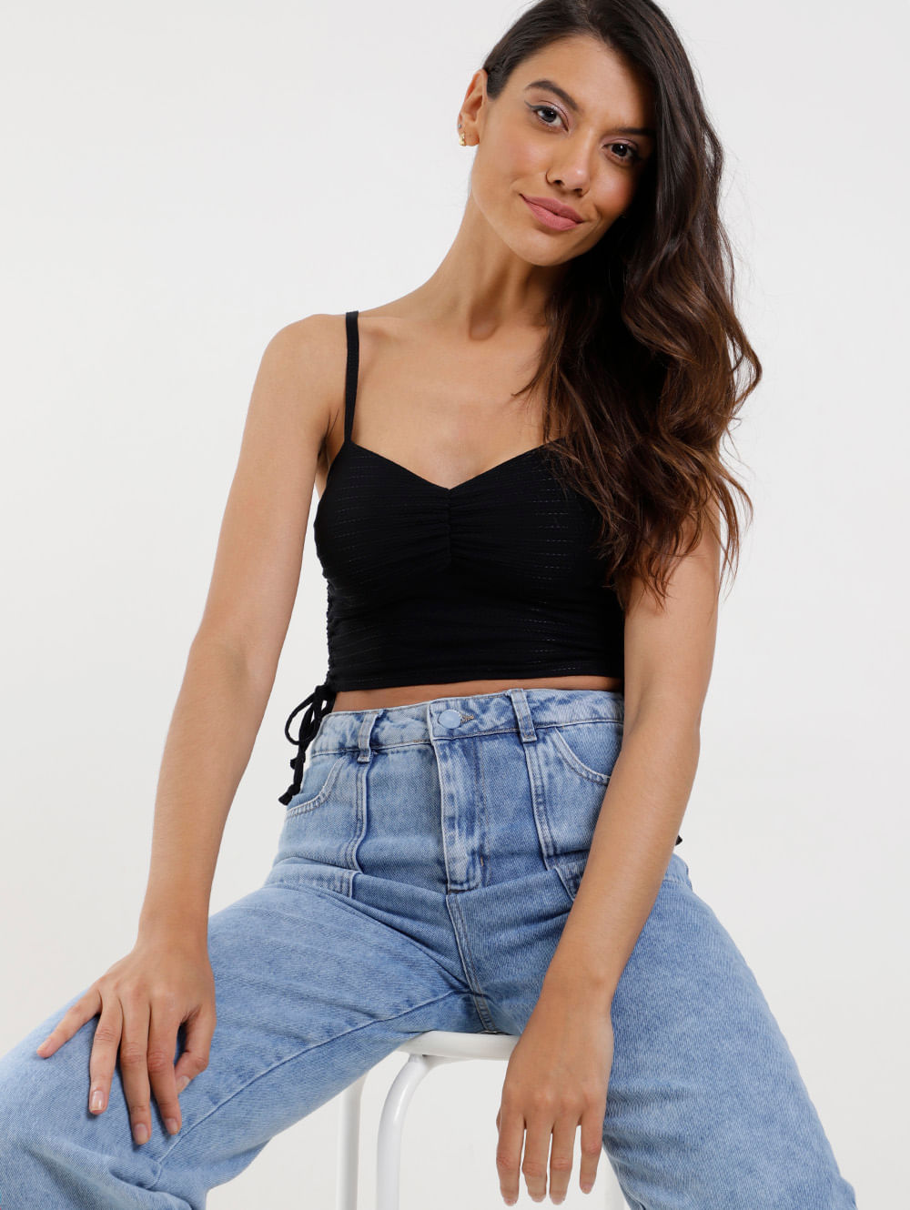 modelo veste um look com cropped preto de alcinha e calça jeans feminina de lavagem clara